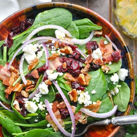 Close overhead shot of a bowl of spinach salad with pecans cranberries and feta cheese