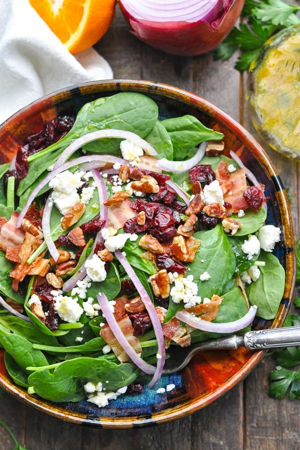 Close overhead shot of a bowl of spinach salad with pecans cranberries and feta cheese