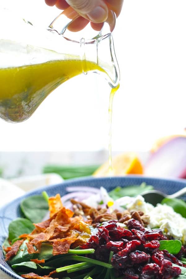 Pouring winter salad dressing over a bowl of spinach greens