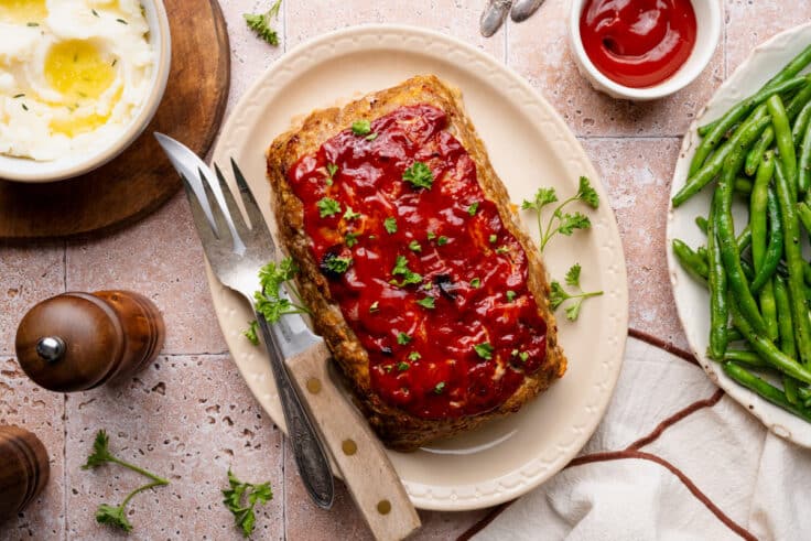 Horizontal overhead shot of a ground turkey meatloaf on an oval white platter with a garnish of minced fresh parsley.