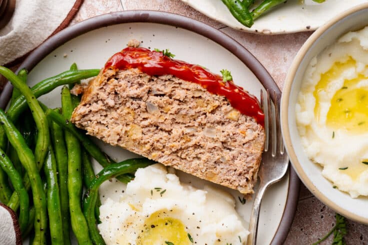 Horizontal overhead image of a slice of ground turkey meatloaf on a plate with a side of mashed potatoes and green beans.