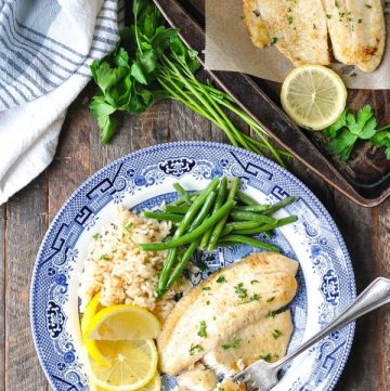 Overhead image of baked tilapia with lemon and garlic on a blue and white plate