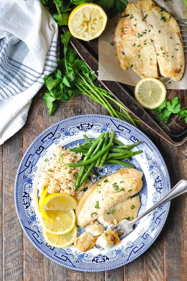 Overhead image of baked tilapia with lemon and garlic on a blue and white plate