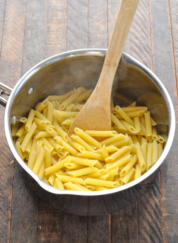 A pot of cooked penne pasta with a wooden spoon.
