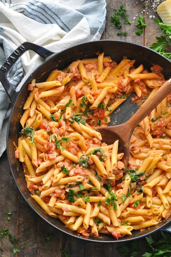 A cast iron skillet filled with penne pasta with spinach and tomatoes.