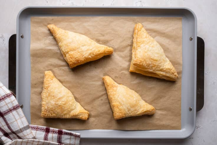 Baked turkey pot pie pockets on a parchment lined baking sheet with a flaky, golden exterior.