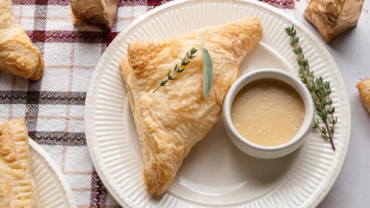 Horizontal overhead shot of turkey pot pie pockets on a white plate with a side of homemade turkey gravy for dipping.