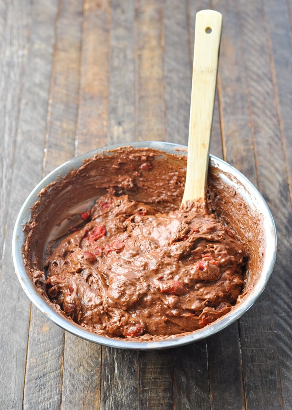 Chocolate cherry cake batter in a mixing bowl with wooden spoon