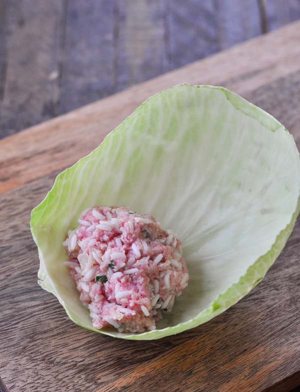 A lump of uncooked stuffed cabbage roll filling sits on a rounded cabbage leaf, ready to be rolled into a cabbage roll.