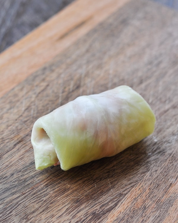 A single, neatly rolled and sealed stuffed cabbage roll sits on a wooden cutting board.