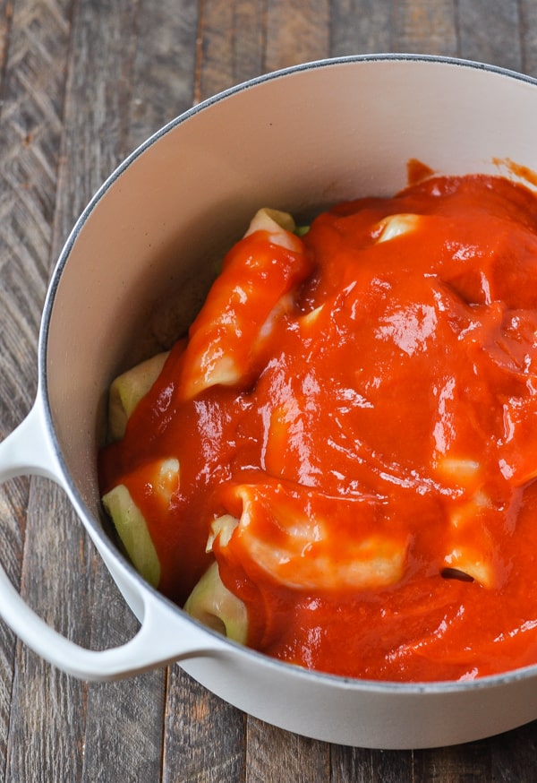 Campbell's condensed tomato soup spread evenly over stacked cabbage rolls in a large, white Dutch oven.
