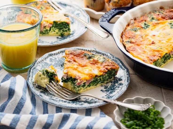 Horizontal side shot of a slice of crustless spinach quiche on a plate with a side of orange juice.