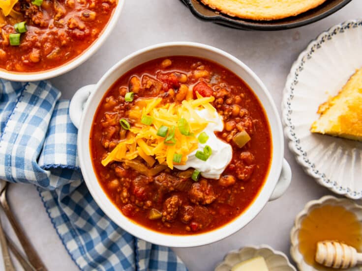 Horizontal overhead shot of a spoon in a bowl of Southern chili with sour cream, cheese, and green onions on top.