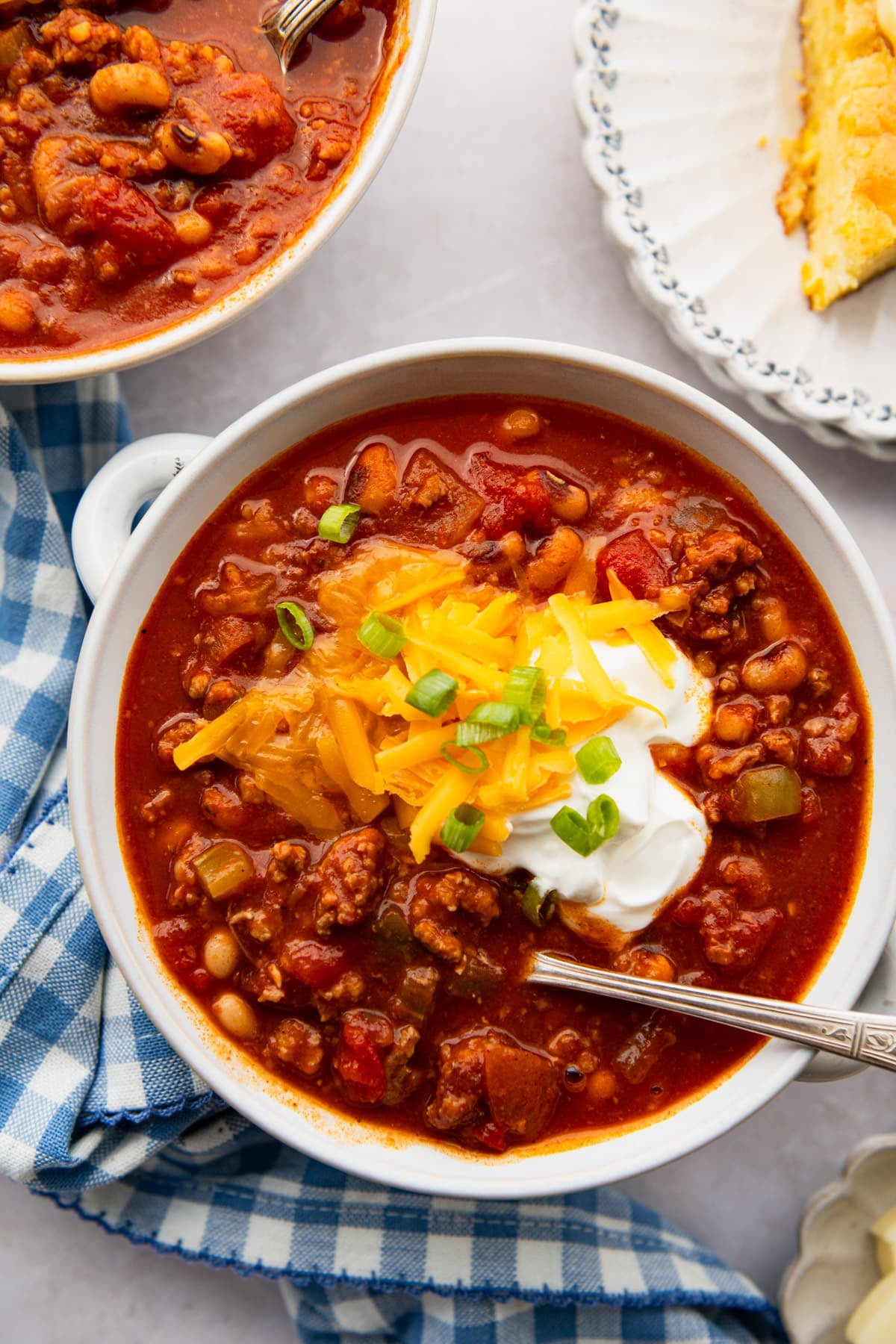 Overhead shot of a spoon in a bowl of Southern chili with sour cream, cheese, and green onions on top.