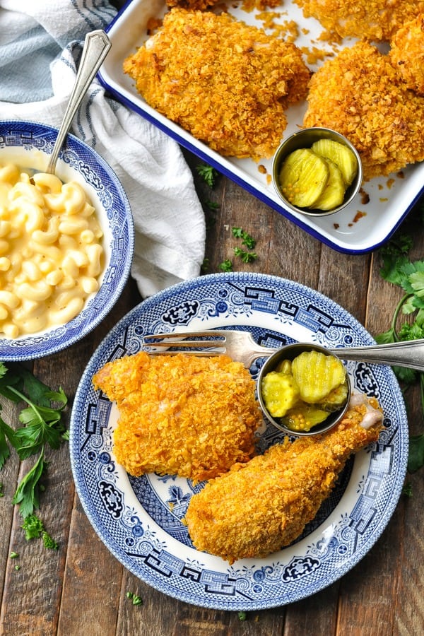 Close overhead shot of Cornflake Chicken on a wooden table with pickles and mac and cheese