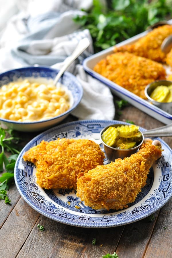 Cornflake Chicken pieces served on a plate with a bowl of mac and cheese in the background