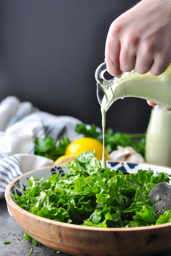 Pouring green goddess dressing over a green salad