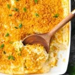 Close overhead shot of cheesy potato casserole in a white dish with wooden serving spoon