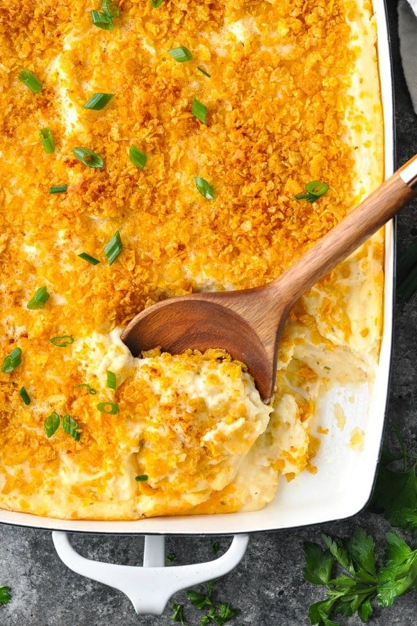 Close overhead shot of cheesy potato casserole in a white dish with wooden serving spoon