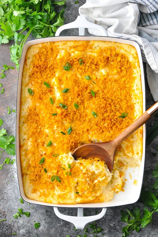 Pan of funeral potatoes on a gray surface with parsley and fresh chives