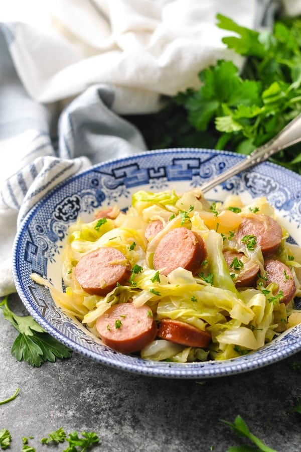 Bowl of sausage and cabbage on a gray surface garnished with fresh parsley