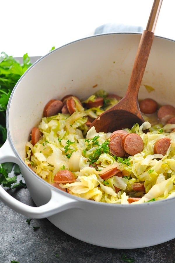 Front shot of sausage and cabbage skillet with wooden spoon