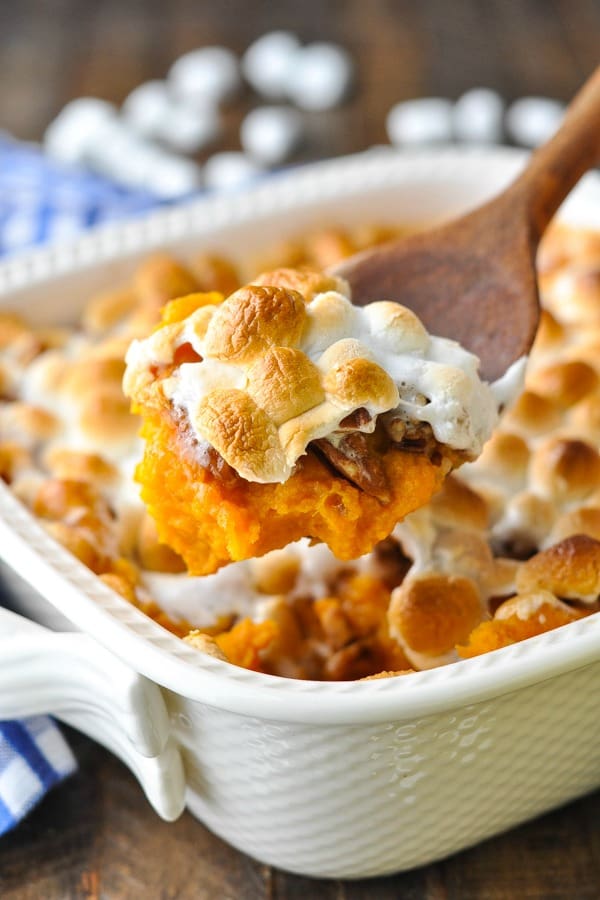Close up front shot of a big scoop of sweet potato casserole with pecans and marshmallows on a wooden spoon