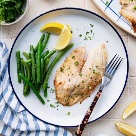 Square overhead shot of a baked tilapia recipe served on a plate of green beans.