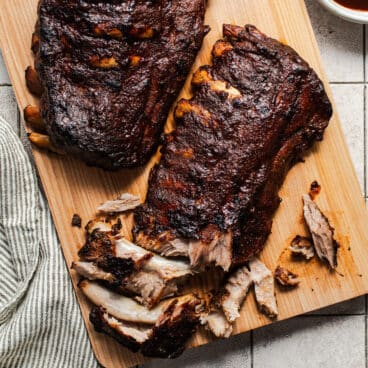 Square overhead image of slow cooker baby back ribs on a wooden cutting board.