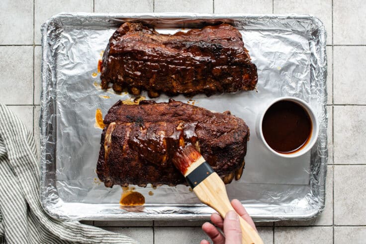 Basting baby back ribs with bbq sauce.