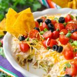 Front shot of 7 layer bean dip in a white dish with tortilla chips in it