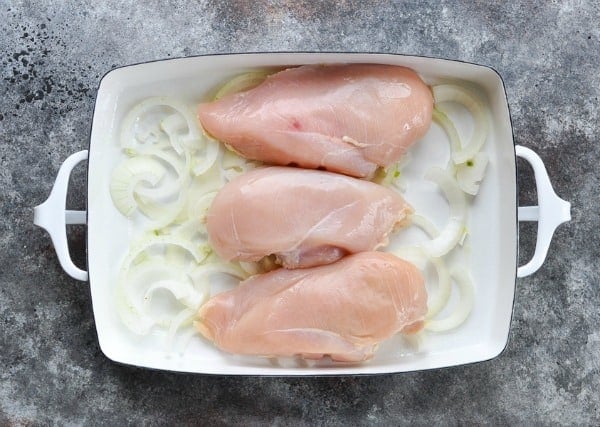 Boneless skinless chicken breasts on top of sliced onion in a baking dish