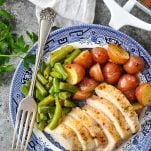 Close up overhead image of sliced baked chicken and potatoes with green beans on a blue and white plate