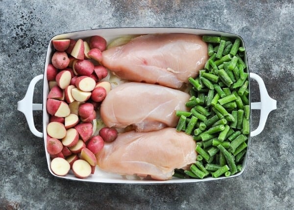 Baby red potatoes with chicken breasts and frozen green beans in a white baking dish
