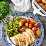 Close overhead shot of one pan chicken and potatoes with green beans on a plate on a gray surface