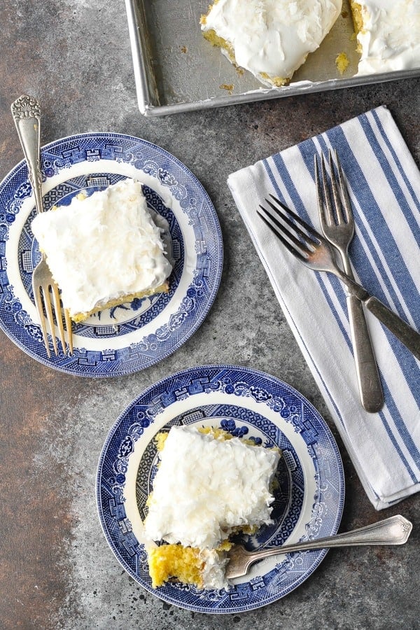 Two slices of coconut cream cake served on plates with forks, next to a cake pan.