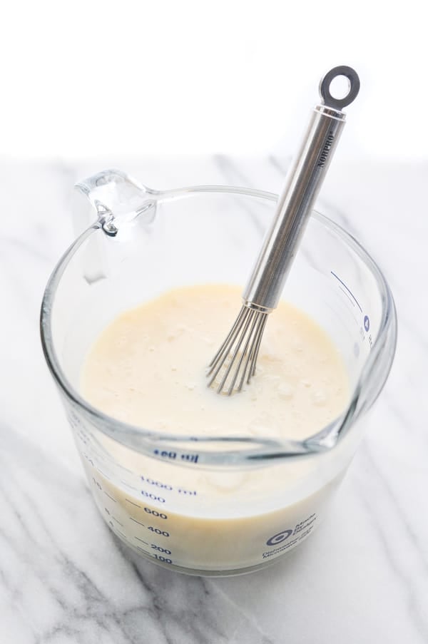 Coconut cream cake filling, made with sweetened condensed milk and cream of coconut, mixed together in a glass measuring cup with a small whisk.