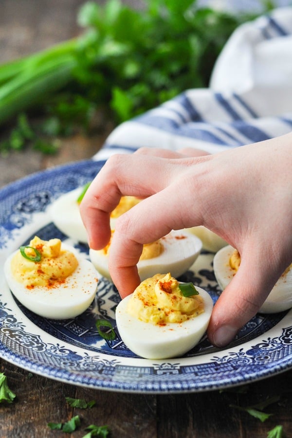 Fingers picking up a deviled egg from a plate