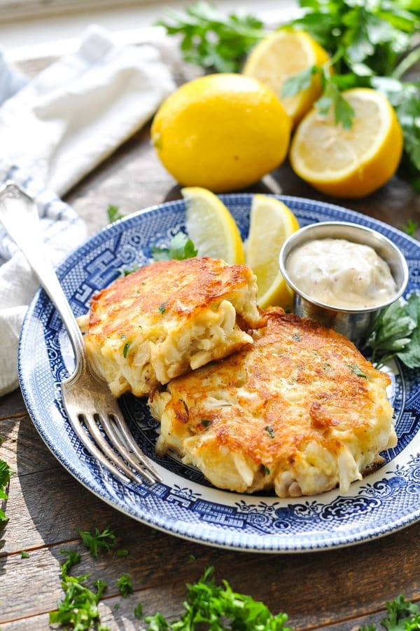 Two crab cakes on a plate with lemon wedges