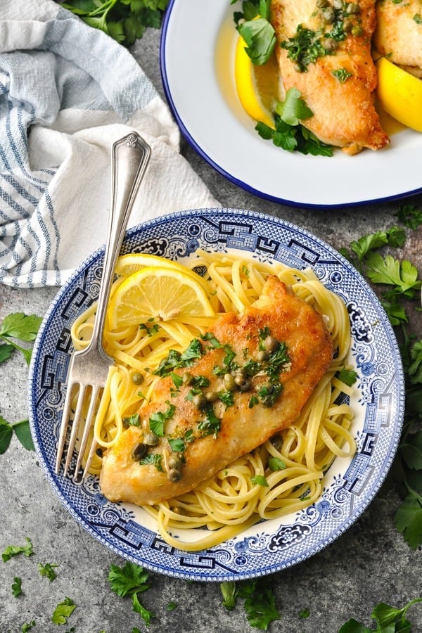 Overhead image of browned chicken cutlet served with a traditional piccata sauce over noodles