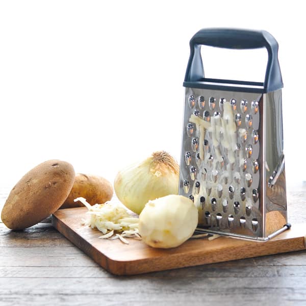 Grating potatoes and onion on a box grater and wooden cutting board