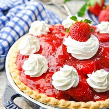 Fresh old fashioned strawberry pie recipe on a white wooden surface garnished with whipped cream