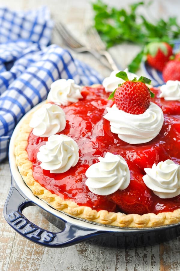 Fresh old fashioned strawberry pie recipe on a white wooden surface garnished with whipped cream