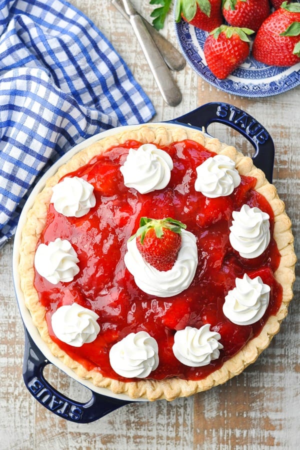 Overhead shot of an old fashioned strawberry pie on a white wooden surface with fresh berries nearby