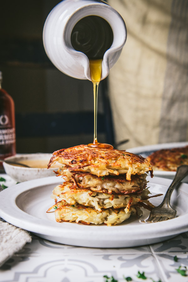 Pouring maple syrup on a stack of crispy potato pancakes
