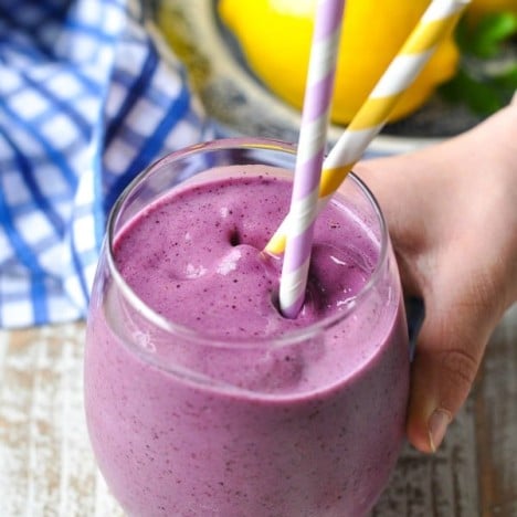 Child's hand holding a banana blueberry smoothie in a glass