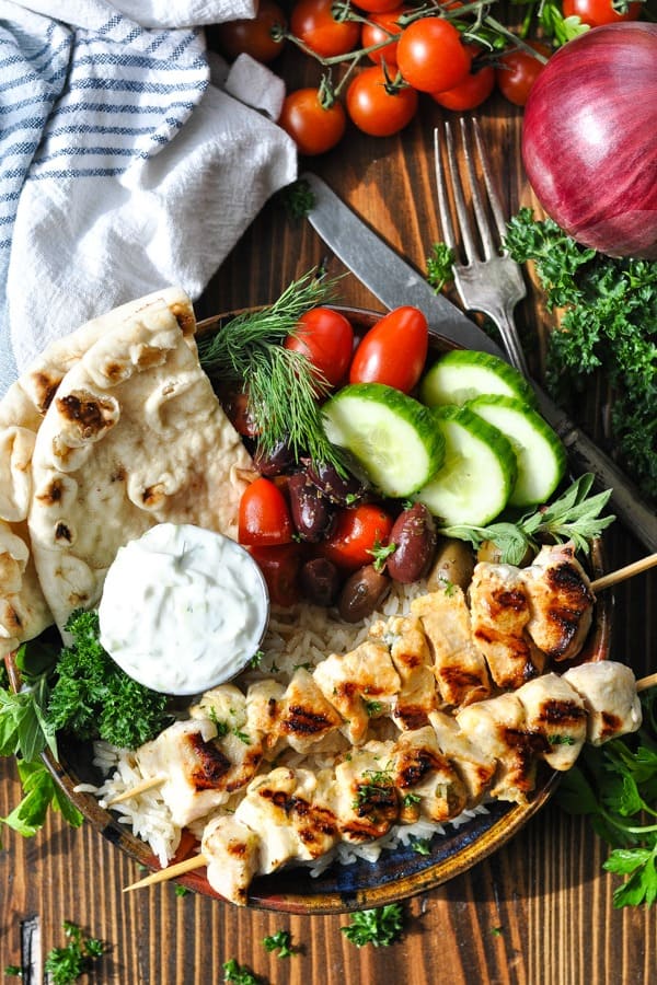 Chicken souvlaki in a bowl with fresh vegetables and tzatziki sauce and pita