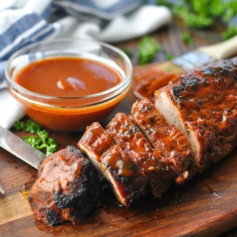Grilled pork tenderloin on a wooden cutting board and basted with barbecue sauce