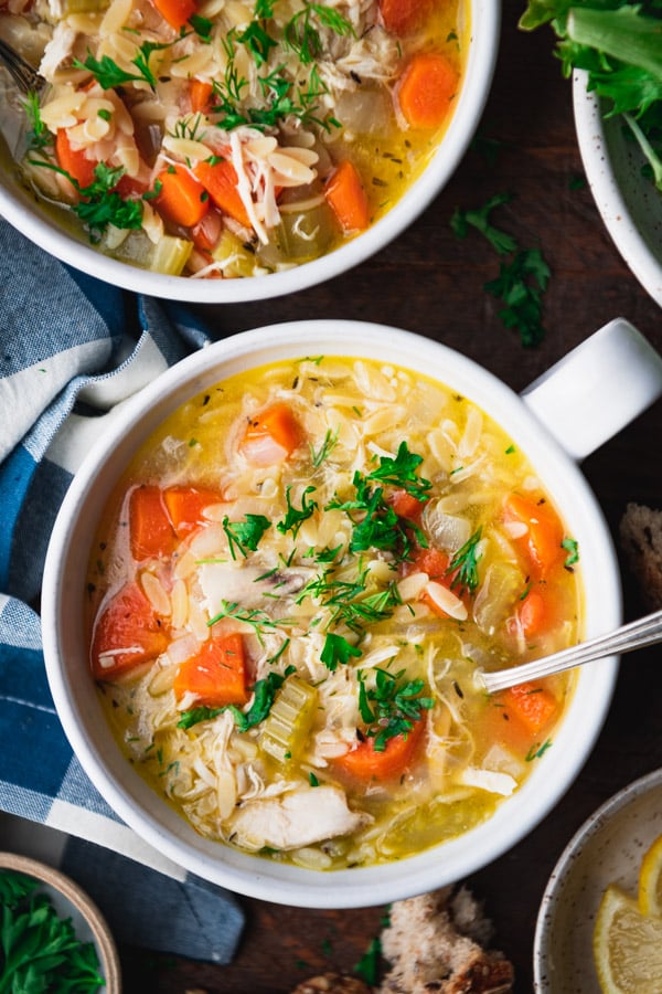 Close overhead image of lemon chicken orzo soup in a white bowl on a table.