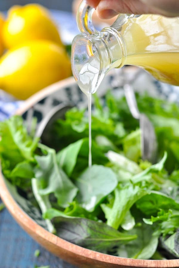 Front shot of pouring lemon vinaigrette dressing on a salad